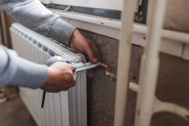 Plumber adjusting radiator connection using a wrench in a room. -repair heating system