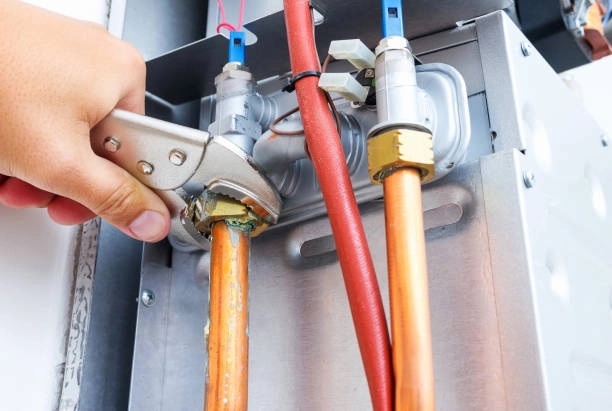 Technician using wrench to tighten copper pipe connection on HVAC unit. -heating system installation