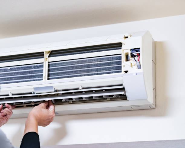 Hands repairing or maintaining a wall-mounted air conditioning unit. -ac service repair