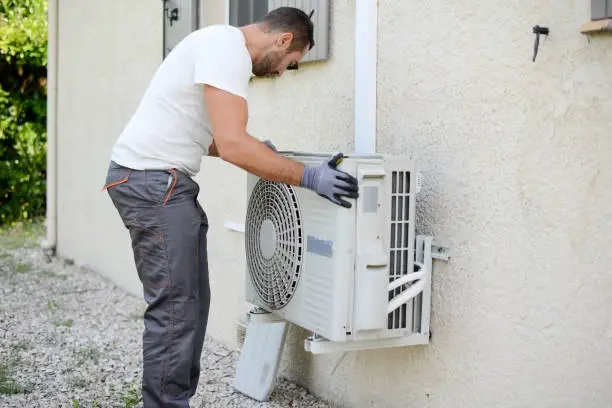 Technician installs outdoor air conditioning unit on residential building wall. -aircon home installation