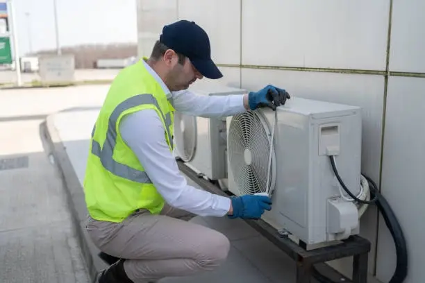 Technician performing maintenance on outdoor air conditioning unit near building wall. -aircon installation services